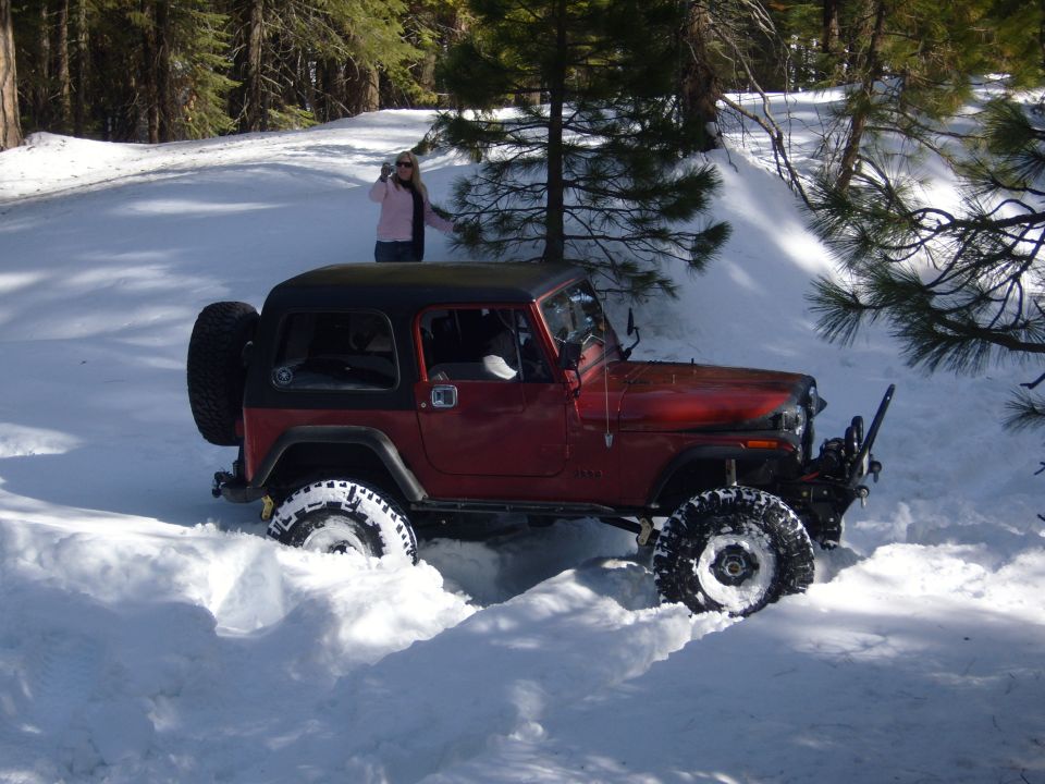 Red 1985 Jeep CJ7 with a black hardtop driving through deep snow, a woman stands in the background