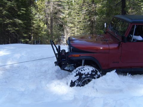 1985 Jeep CJ7 - A Jeep is partially buried in snow, with a winch cable extending from its front.