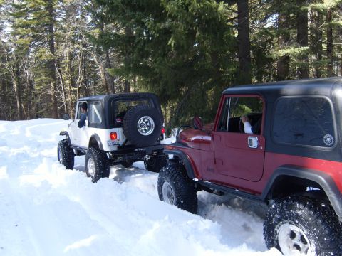 1985 Jeep CJ7 - Two Jeep CJ-series vehicles are shown driving through a snow-covered forest path.