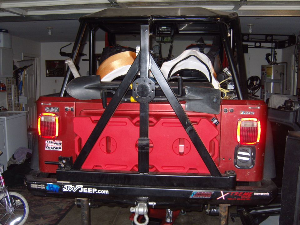 Red 1985 Jeep CJ7 rear view with spare tire carrier, jerry cans, and shovels