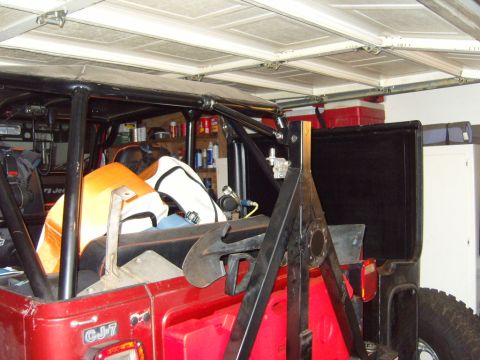 1985 Jeep CJ7 - Rear view of a red Jeep CJ-7 with a roll cage and spare tire carrier, parked inside a garage.