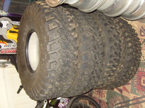 1985 Jeep CJ7 - A stack of four large off-road tires are visible, with one tire showing its white rim.