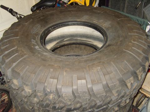 1985 Jeep CJ7 - Several large off-road tires are stacked, with the tread pattern prominently visible on the top tire.