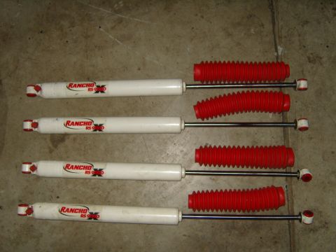 1985 Jeep CJ7 - Four Rancho RS 9000 shock absorbers with red boots are laid out on a concrete surface.