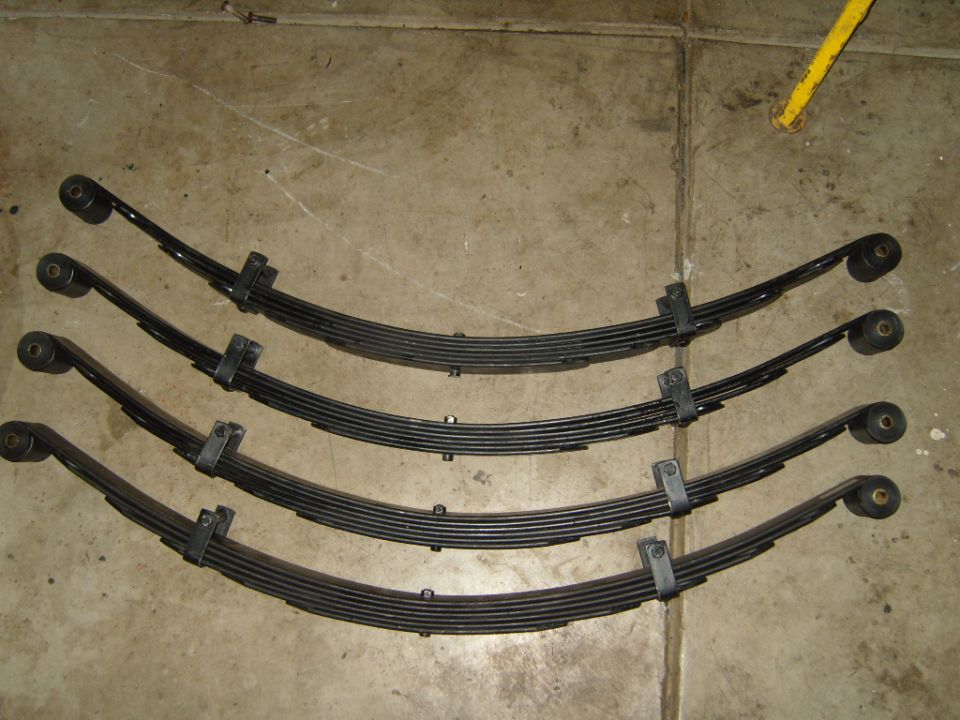 Four leaf springs laid out on a concrete floor. Supermotors.net logo visible