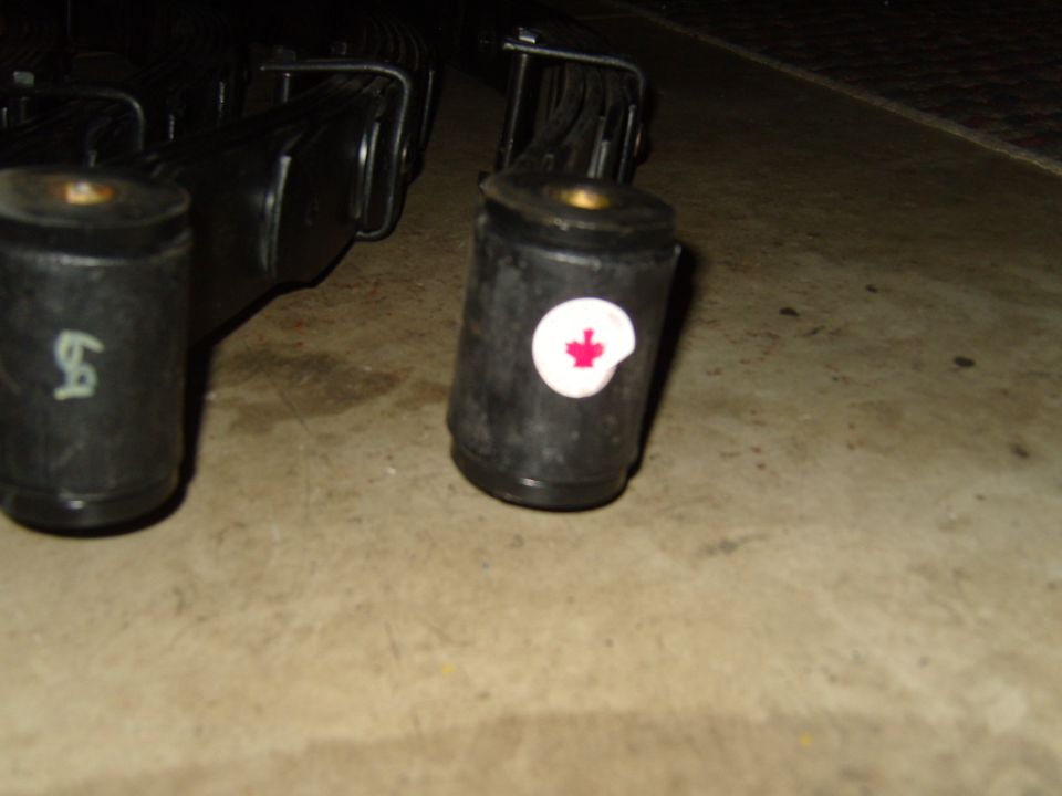 close up of two black leaf spring bushings, one has a white circle with a red maple leaf emblem