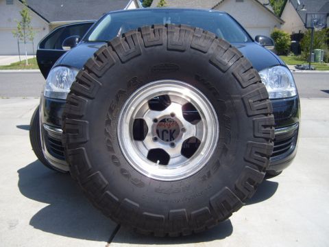 1985 Jeep CJ7 - A large spare tire is mounted in front of a black car, partially obscuring its grille and headlights.
