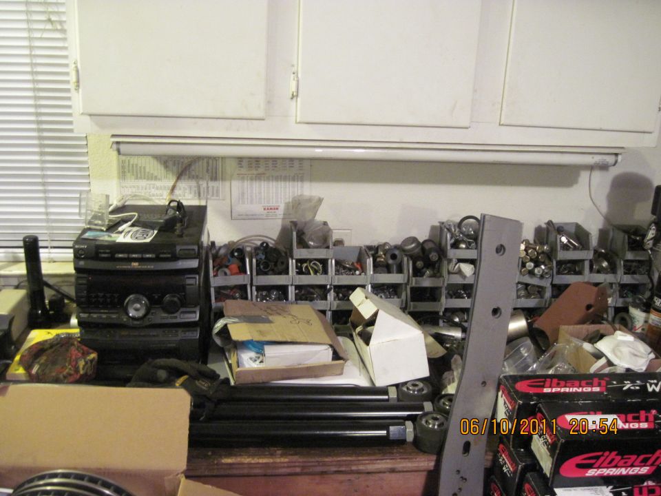 Workbench with stereo, bins of parts, and boxes. Some parts are labeled Eibach Springs