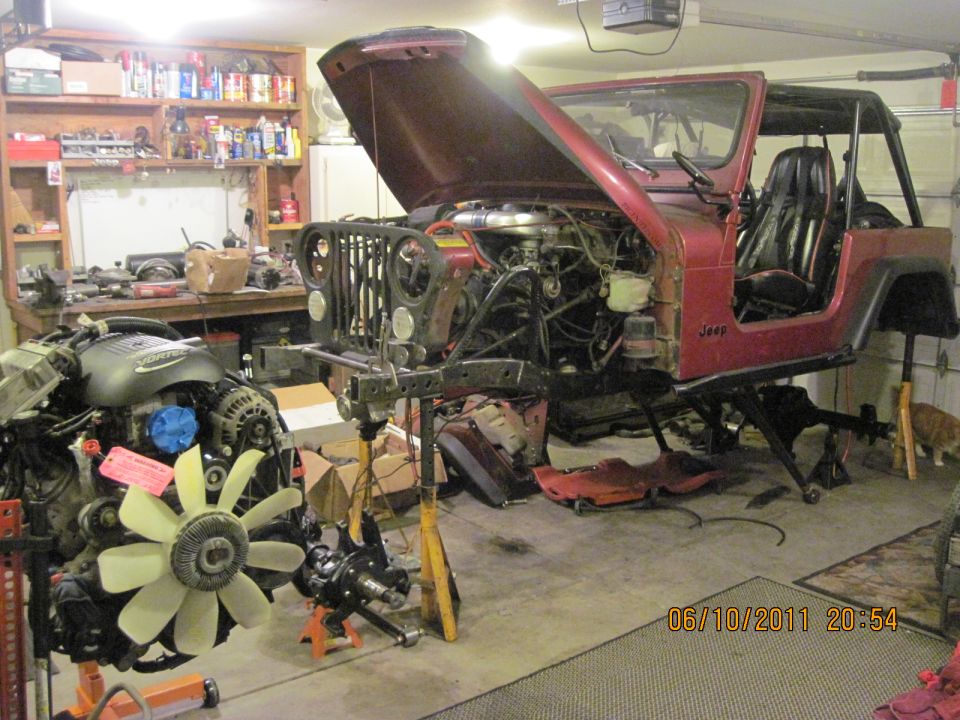 Red Jeep CJ7 with hood open, engine removed, on jack stands in a garage