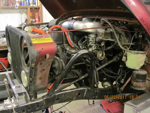 1985 Jeep CJ7 - The engine bay of a red Jeep CJ7 is visible with the hood open, revealing the engine and surrounding components.