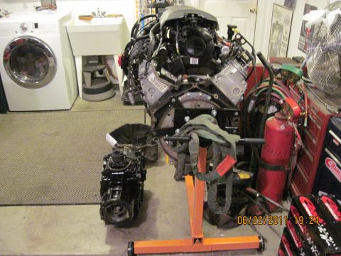 1985 Jeep CJ7 - Engine and transmission assembly displayed in a garage setting, with a washing machine and utility sink visible in the background.