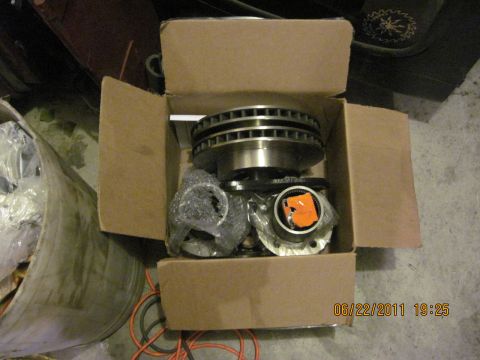 1985 Jeep CJ7 - Box of automotive parts, including brake rotors and hub assemblies, on a concrete floor.