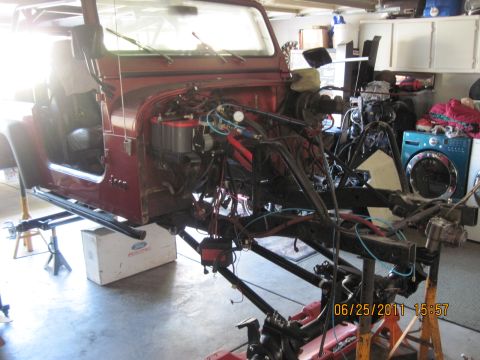 1985 Jeep CJ7 - A red Jeep CJ7 is disassembled and elevated on jack stands in a garage, revealing its internal components.