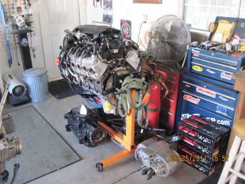1985 Jeep CJ7 - An engine is mounted on an orange engine stand, surrounded by tools and equipment in a garage setting.