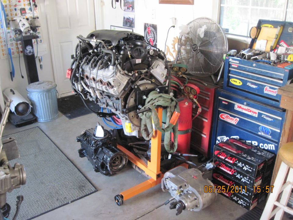 Engine on an orange engine stand in a garage with toolboxes and a fan