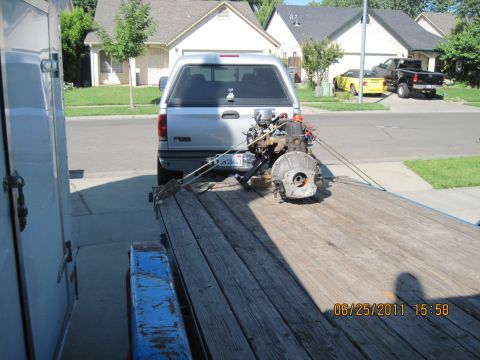 1985 Jeep CJ7 - A pickup truck tows a trailer carrying an engine and transmission, with other vehicles visible in the background.