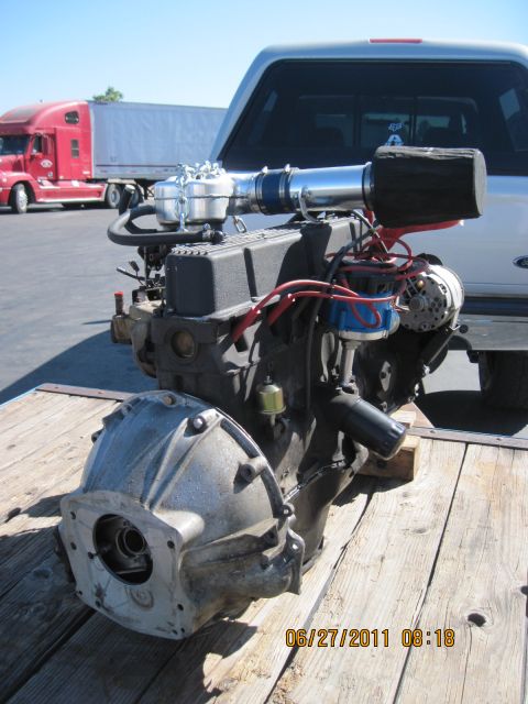 1985 Jeep CJ7 - Engine and transmission assembly on a wooden surface, with a semi-truck in the background.