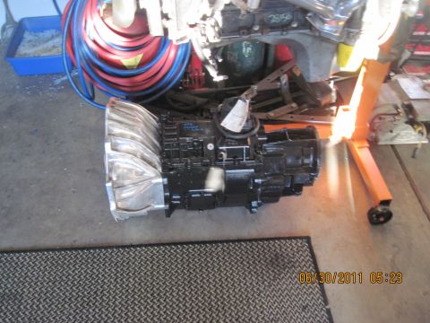 1985 Jeep CJ7 - A black transmission with a silver intake manifold is shown on the floor, with various tools and hoses in the background.