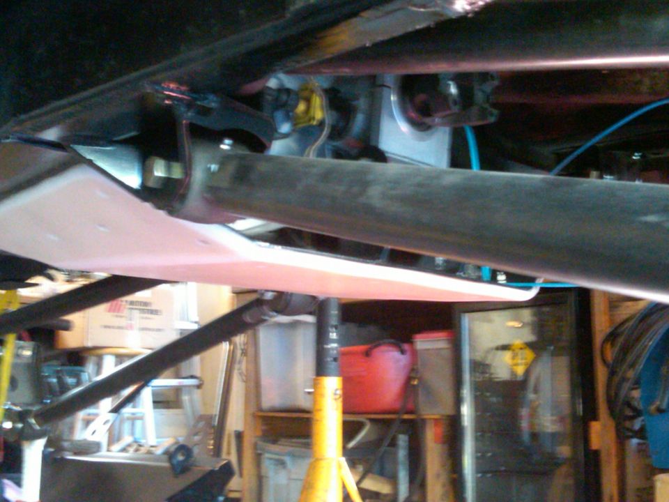 Underside of a vehicle with suspension components and a skid plate visible. It's on jack stands in a garage
