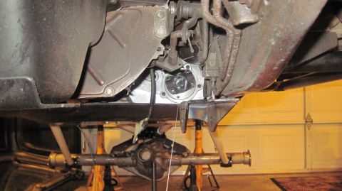 1985 Jeep CJ7 - Underside view of vehicle drivetrain and rear axle supported by jack stands, with a garage door in the background.