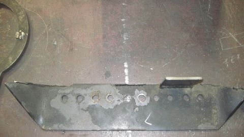 1985 Jeep CJ7 - A metal bracket with a series of holes and a welded tab sits on a workbench surface.