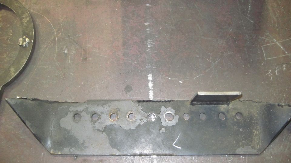metal bracket with multiple holes and a welded tab, on a workbench