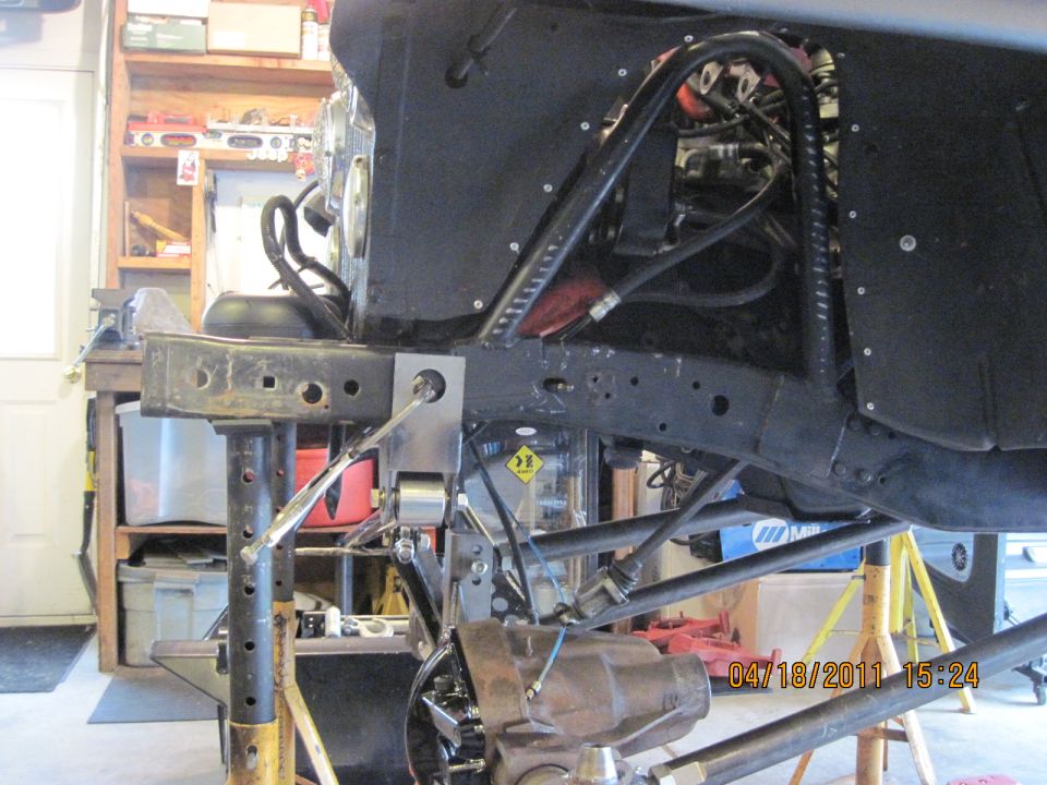 Close-up of a Jeep's frame and suspension system with hydraulic lines and a differential visible. The vehicle is supported by jack stands