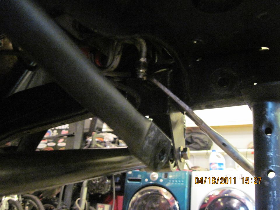 Undercarriage of a vehicle with a large black bar and metal linkage, viewed from below