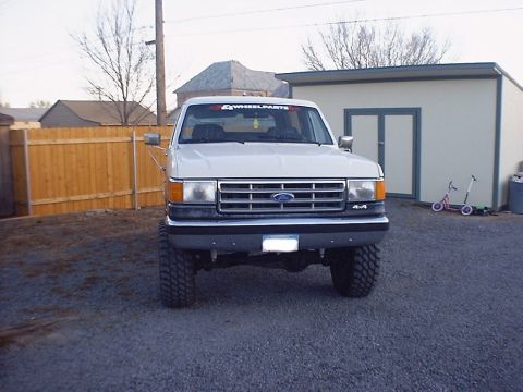 1988 Ford Bronco - This lifted Ford F-Series truck is parked in a gravel driveway next to a wooden fence and a shed.