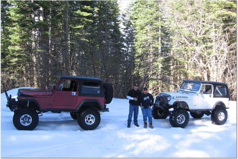 1985 Jeep CJ7 - Two modified Jeep CJ-series vehicles are parked in a snowy forest with two men standing between them.