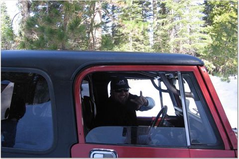 1985 Jeep CJ7 - Man in a red Jeep CJ-series gives a shaka sign while driving through a snowy, wooded area.