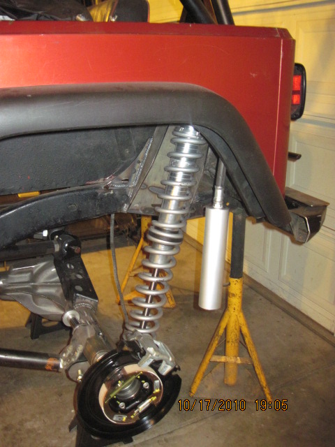1985 Jeep CJ7 - Close-up view of the rear suspension and brake assembly on a red Jeep, showing a coilover shock absorber.