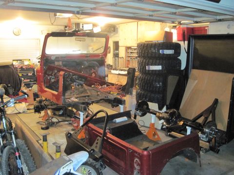 1985 Jeep CJ7 - A red Jeep CJ body is undergoing restoration in a garage, surrounded by various parts and tools.