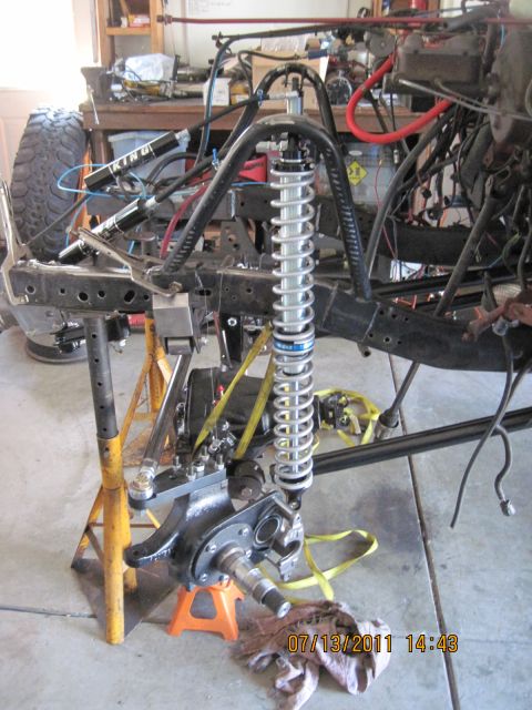 1985 Jeep CJ7 - Close-up of a Jeep CJ frame undergoing modification, showing suspension components and roll cage structure.