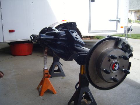 1985 Jeep CJ7 - A rear axle assembly, likely from a Jeep, is shown supported by jack stands in front of a white trailer.