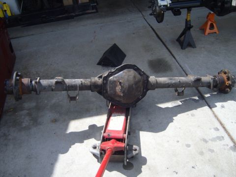 1985 Jeep CJ7 - A disassembled rear axle assembly is supported by a jack, with another vehicle's axle visible in the background.
