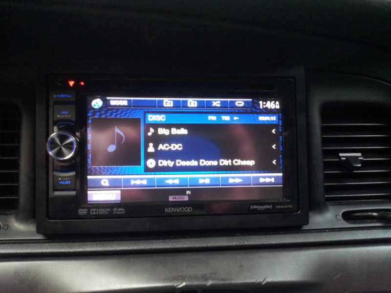 Car interior showing aftermarket Kenwood stereo display with music track list