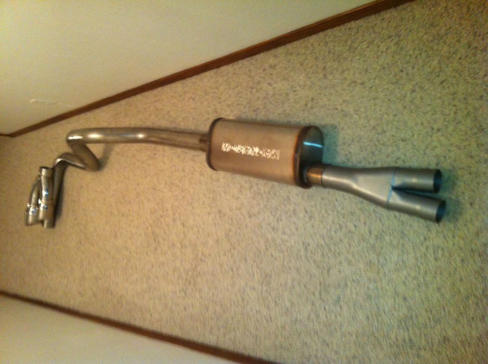 Exhaust system with a cylindrical muffler and dual tailpipes, mounted on a wall