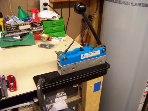 1995 Mercury Grand Marquis - A blue reloading press with a black handle sits on a workbench, surrounded by various tools and supplies.