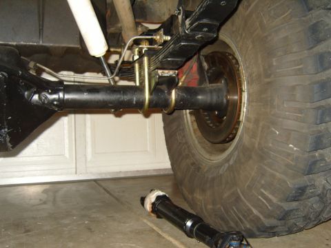 1985 Jeep CJ7 - Close-up of a Jeep's rear axle, leaf springs, and shock absorber, with a driveshaft lying nearby.