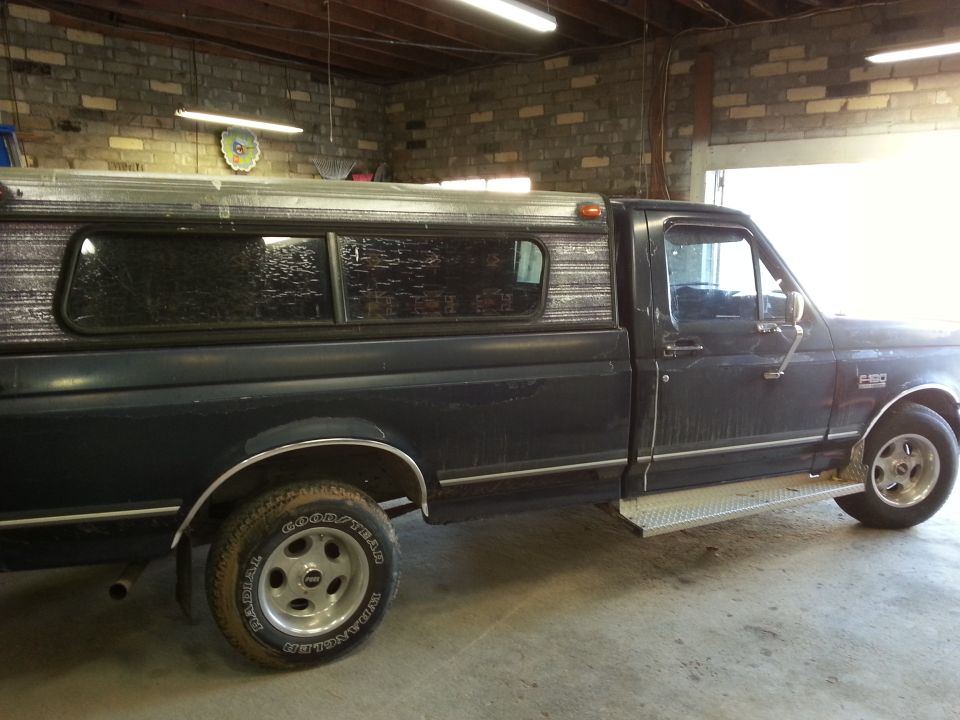 Dark blue pickup truck with a camper shell, side view, showing a step bar and alloy wheels