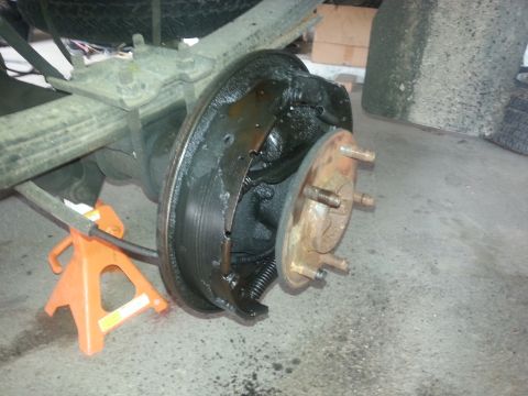 1989 Ford F-150 - The rear drum brake assembly is exposed, with brake shoes and a rusty hub visible. The vehicle is supported by a jack stand.