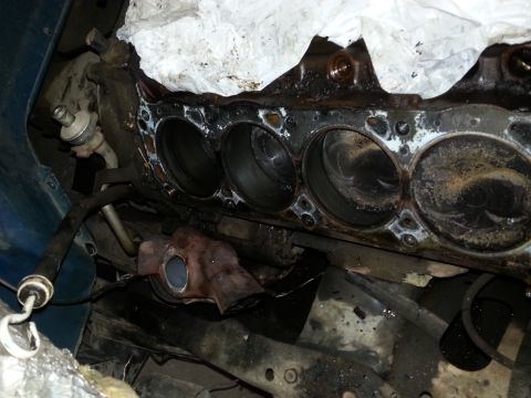 1989 Ford F-150 - Top view of a disassembled engine block with cylinder bores exposed and oily residue, parked vehicle body panels visible above.