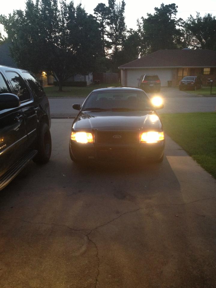 2007 Ford Crown Victoria, dark color, front view, headlights on, parked on driveway next to a black SUV