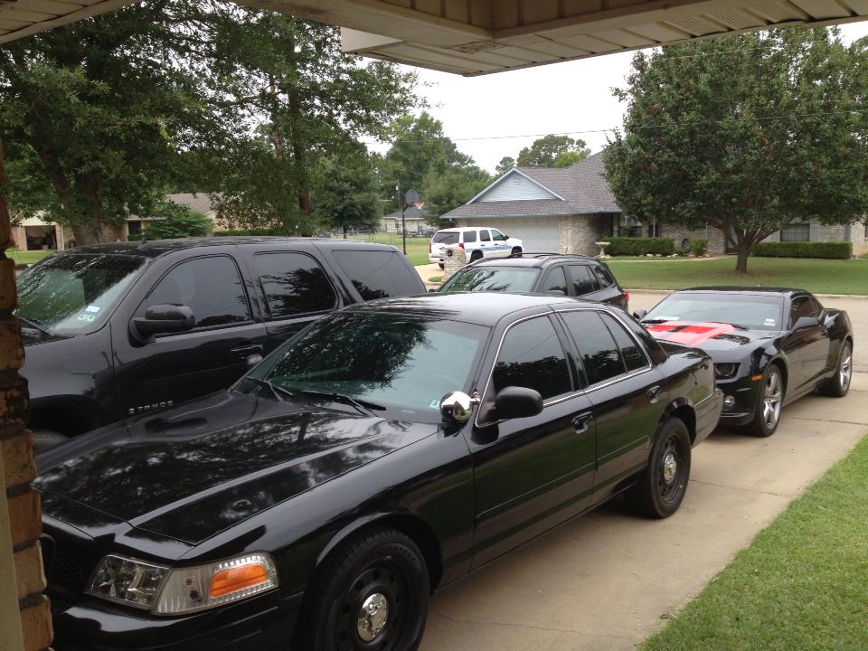 2007 Ford Crown Victoria police car parked next to a black Chevrolet Camaro and a black SUV