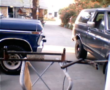 1991 Ford Bronco - A length of steel tubing clamped across a folding sawhorse-style work stand in a driveway, part of a bumper or brush-guard fabrication job.…