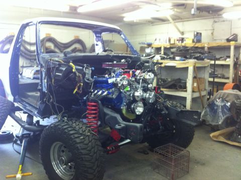 1982 Ford Bronco - A white Ford Bronco is disassembled in a workshop, showing its engine and suspension components.
