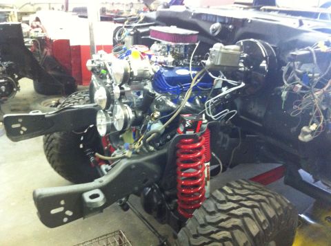 1982 Ford Bronco - The engine and chassis of a 1982 Ford Bronco are visible, red coilover suspension and custom engine components.