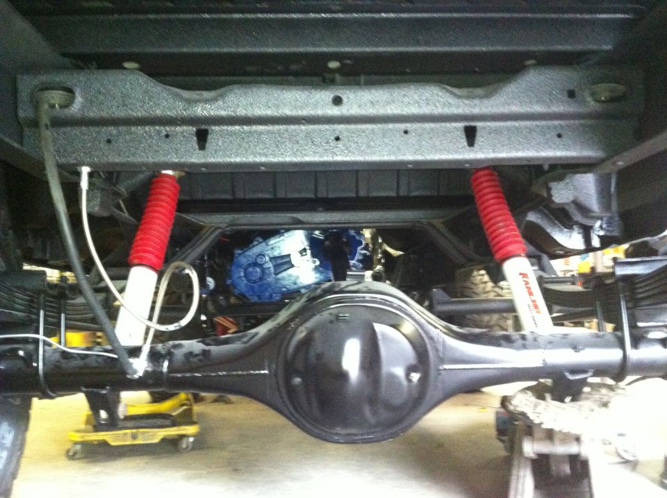 Underside view of a vehicle's rear axle, differential, leaf springs, and red shock absorbers