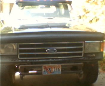 1991 Ford Bronco - Front view of a dark late-1980s Ford truck in a driveway, showing the horizontal-bar grille with blue Ford oval, rectangular headlights, an…